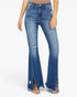 A model wearing medium-wash blue denim flare jeans with distressed details and side slits, paired with clear high-heel sandals against a plain white background.