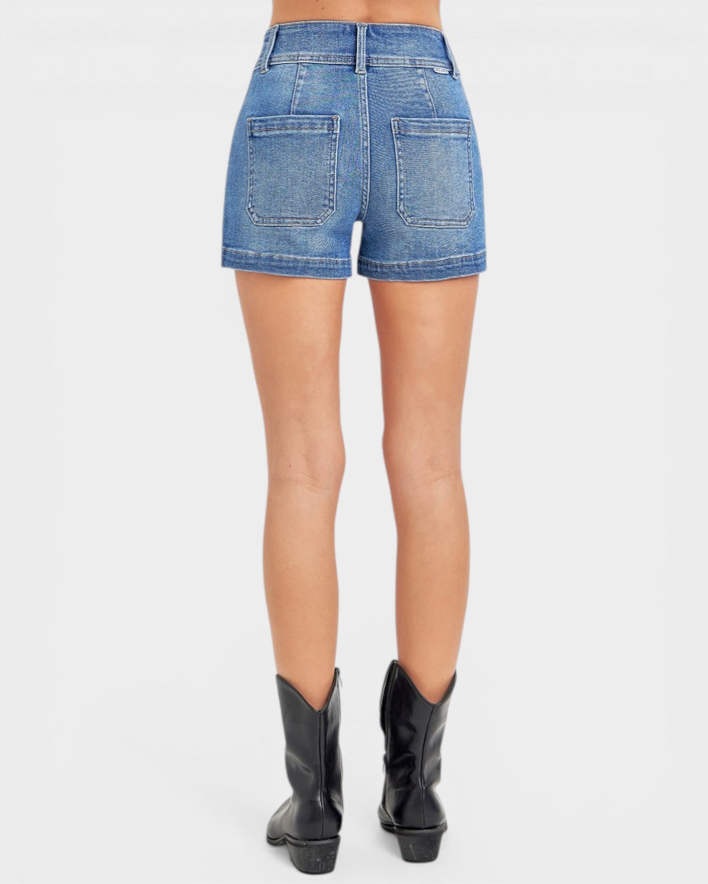 Person wearing blue denim shorts and black cowboy boots on a white background