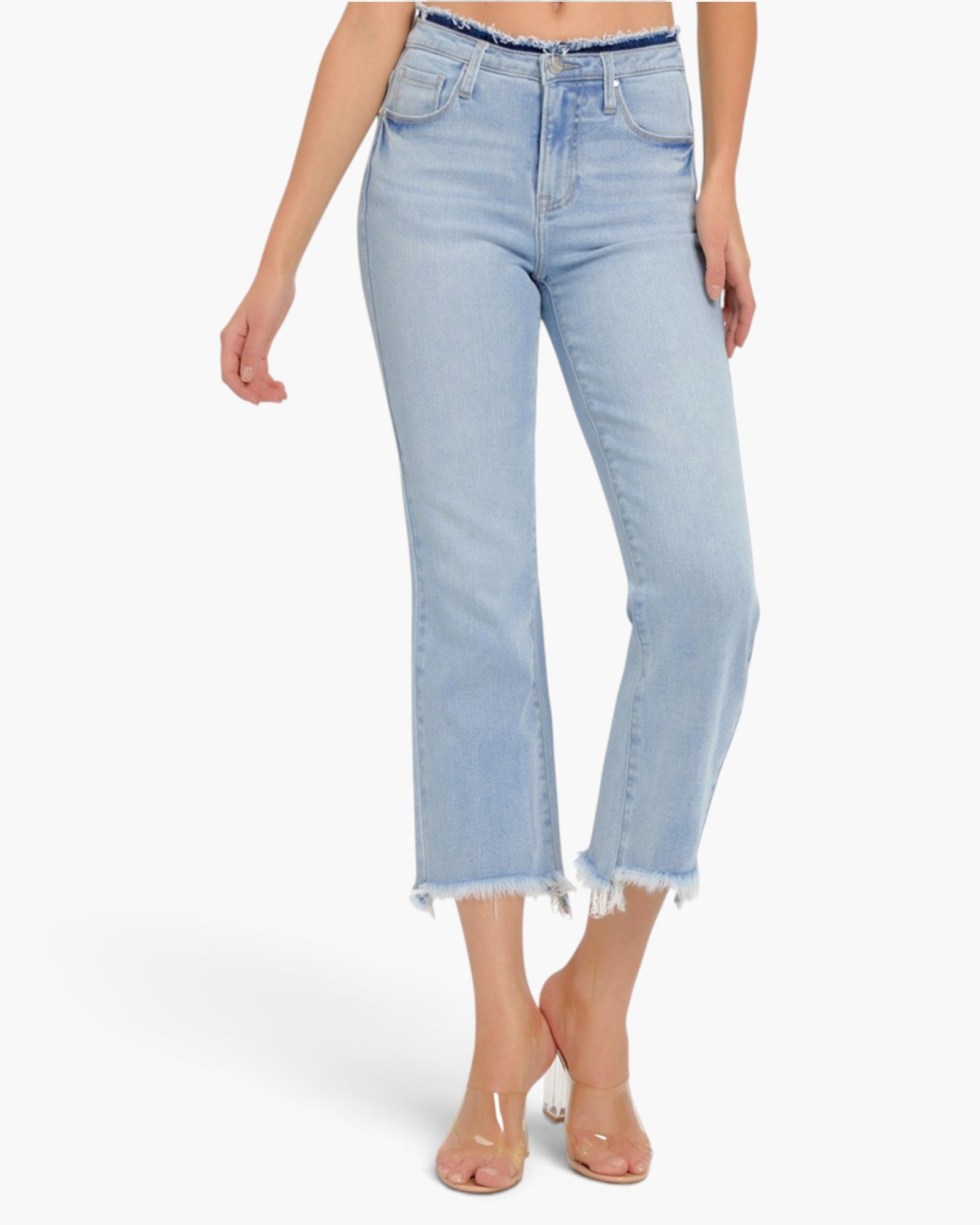 A model wearing light-wash blue cropped jeans with a frayed hem and a dark patterned waistband, paired with clear high-heeled sandals against a plain white background.