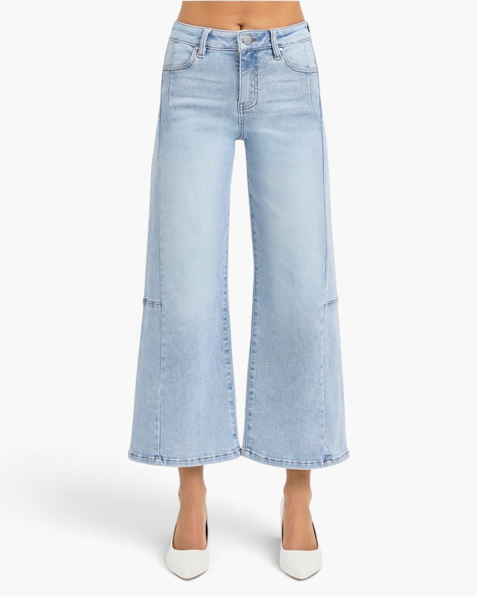 A model wearing light-wash blue wide-leg cropped jeans with front patch pockets, paired with white pointed-toe heels, shown against a plain light gray studio background.