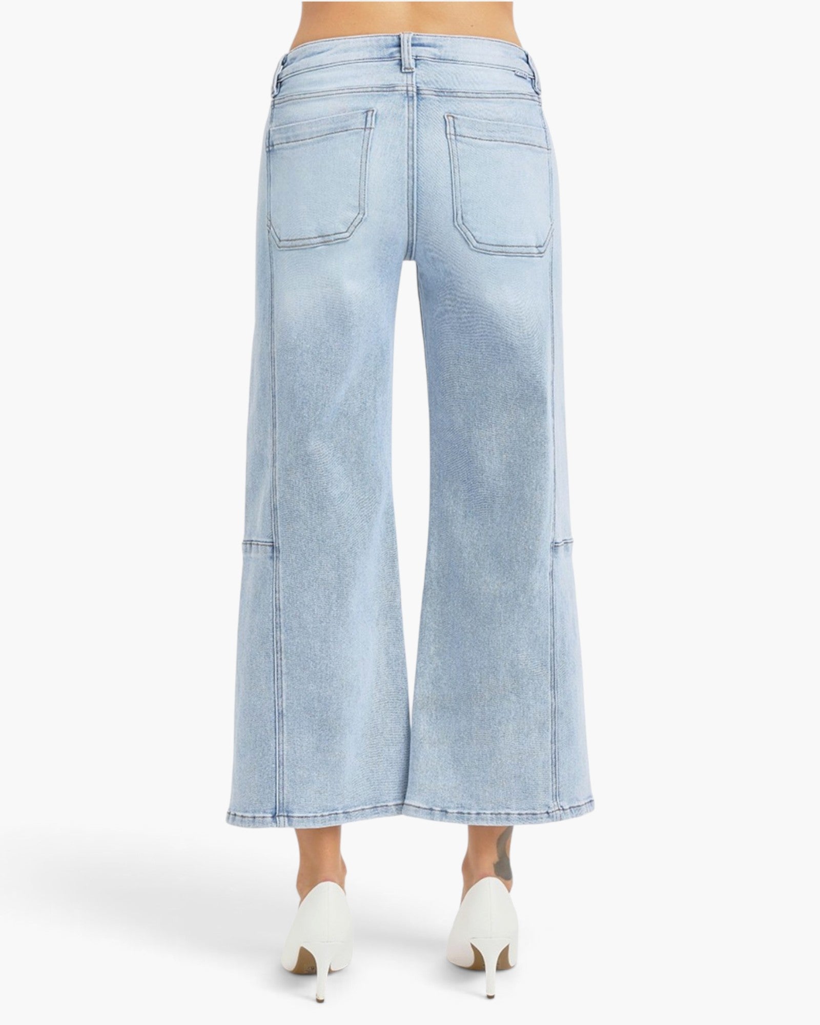 Light blue wide-leg denim jeans shown from the back on a model, paired with white pointed-toe heels against a plain white studio background.