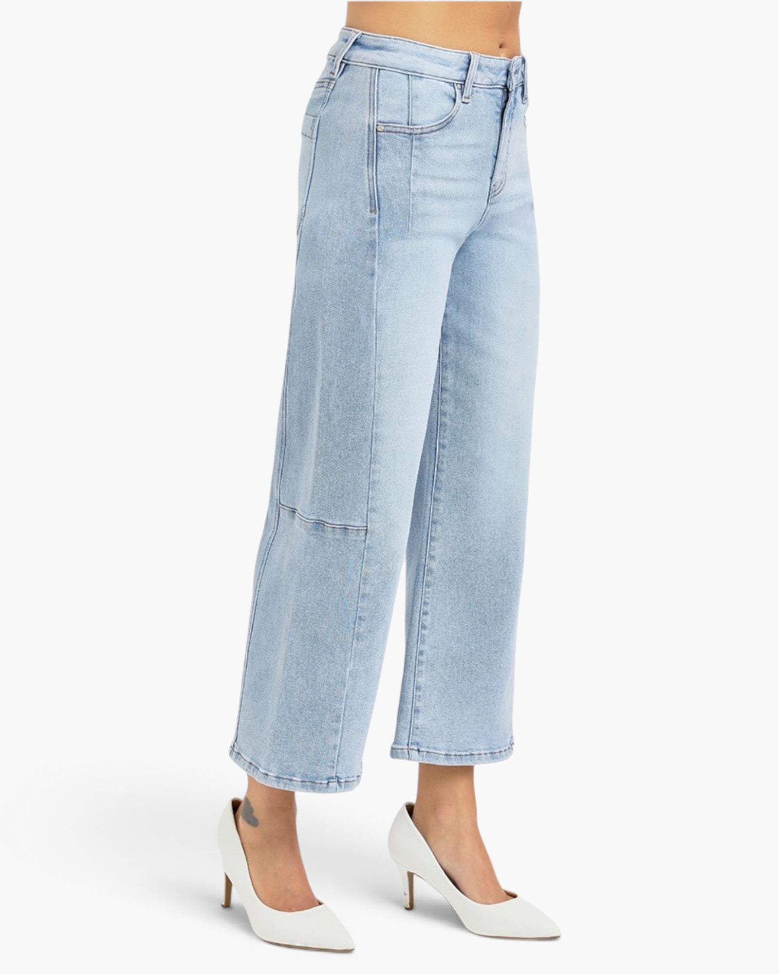 A model is shown from the waist down wearing light-wash blue cropped wide-leg jeans with patch pockets and white pointed-toe heels, set against a plain white studio background.