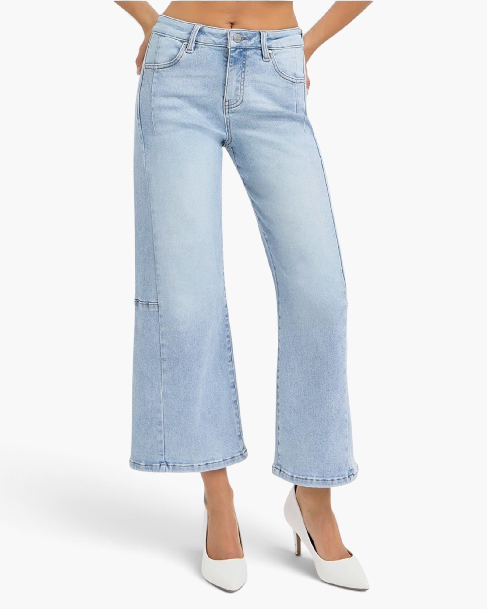 A model wearing light-wash blue cropped wide-leg denim jeans with front patch pockets and white pointed-toe heels, shown against a clean white studio background.