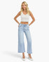 A blonde model wearing a white ribbed crop top, light-wash wide-leg cropped jeans, and white pointed-toe heels, standing against a light gray studio background.