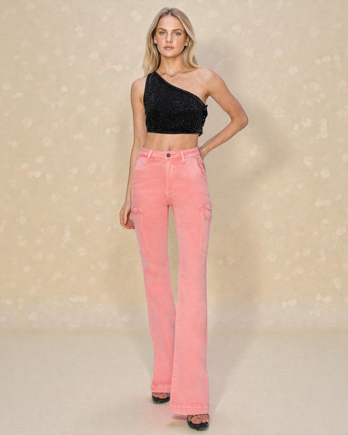 Woman wearing a black one-shoulder top and pink jeans on a beige background