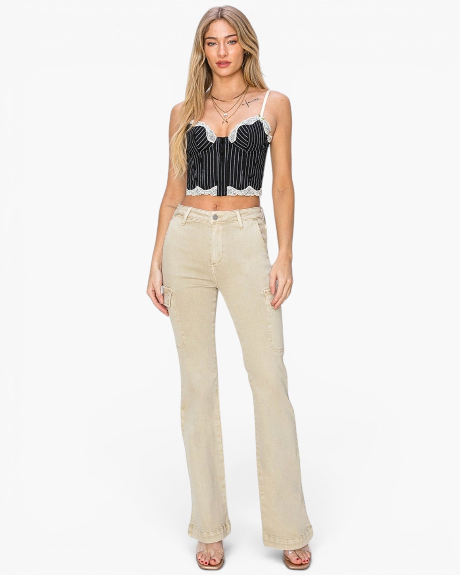 A woman modeling a black and white striped crop top with white lace trim and beige high-waisted flared jeans against a plain white background.