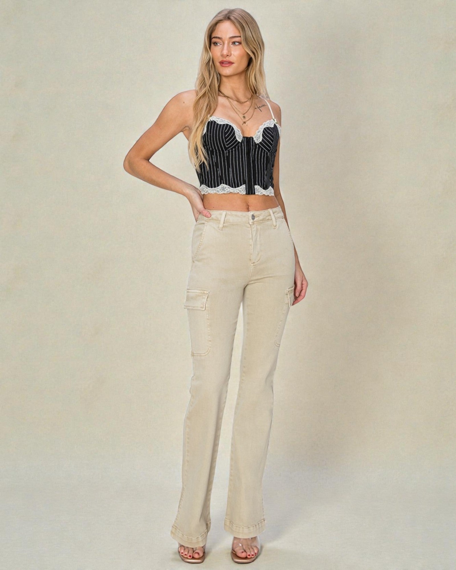 Woman wearing a black and white striped crop top and beige flared jeans on a plain background