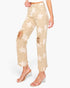A model wears beige cropped jeans with a white star pattern and distressed rips on the knees, paired with clear high-heeled sandals, against a plain white background.