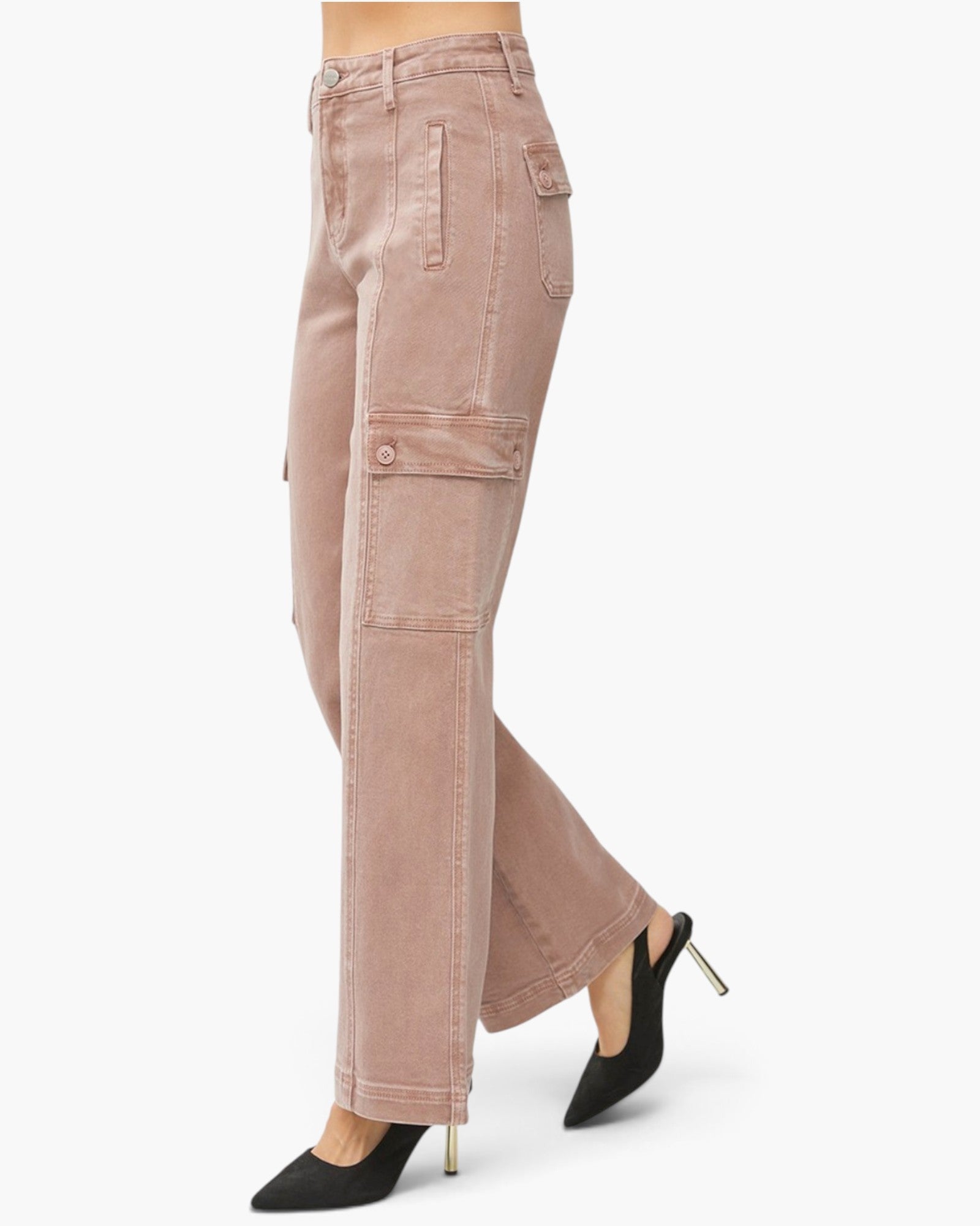 A side profile view of a person wearing dusty rose cargo jeans and black pointed-toe high heels with gold stiletto heels, set against a plain white studio background.