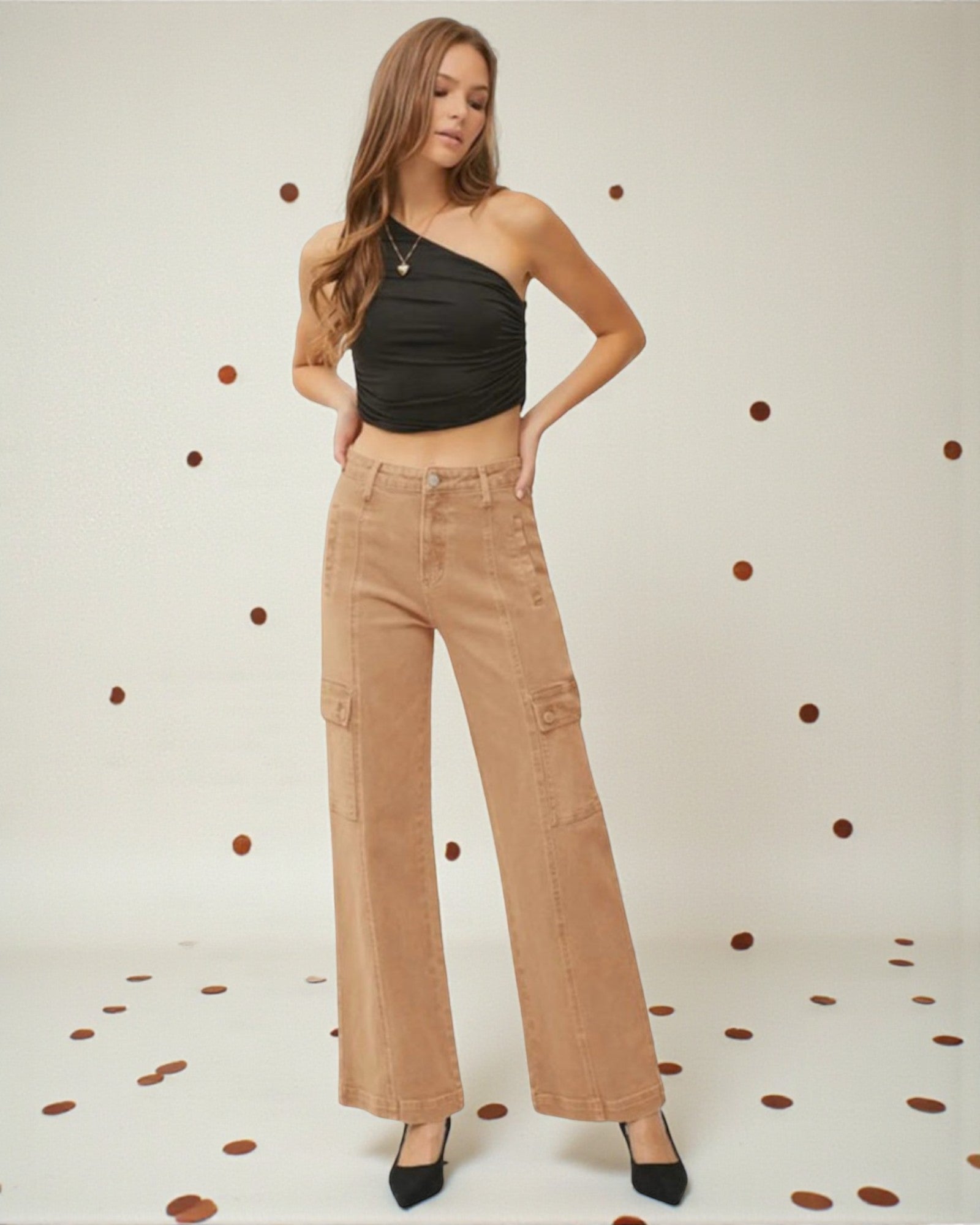 Woman wearing a black top and beige pants against a polka dot background