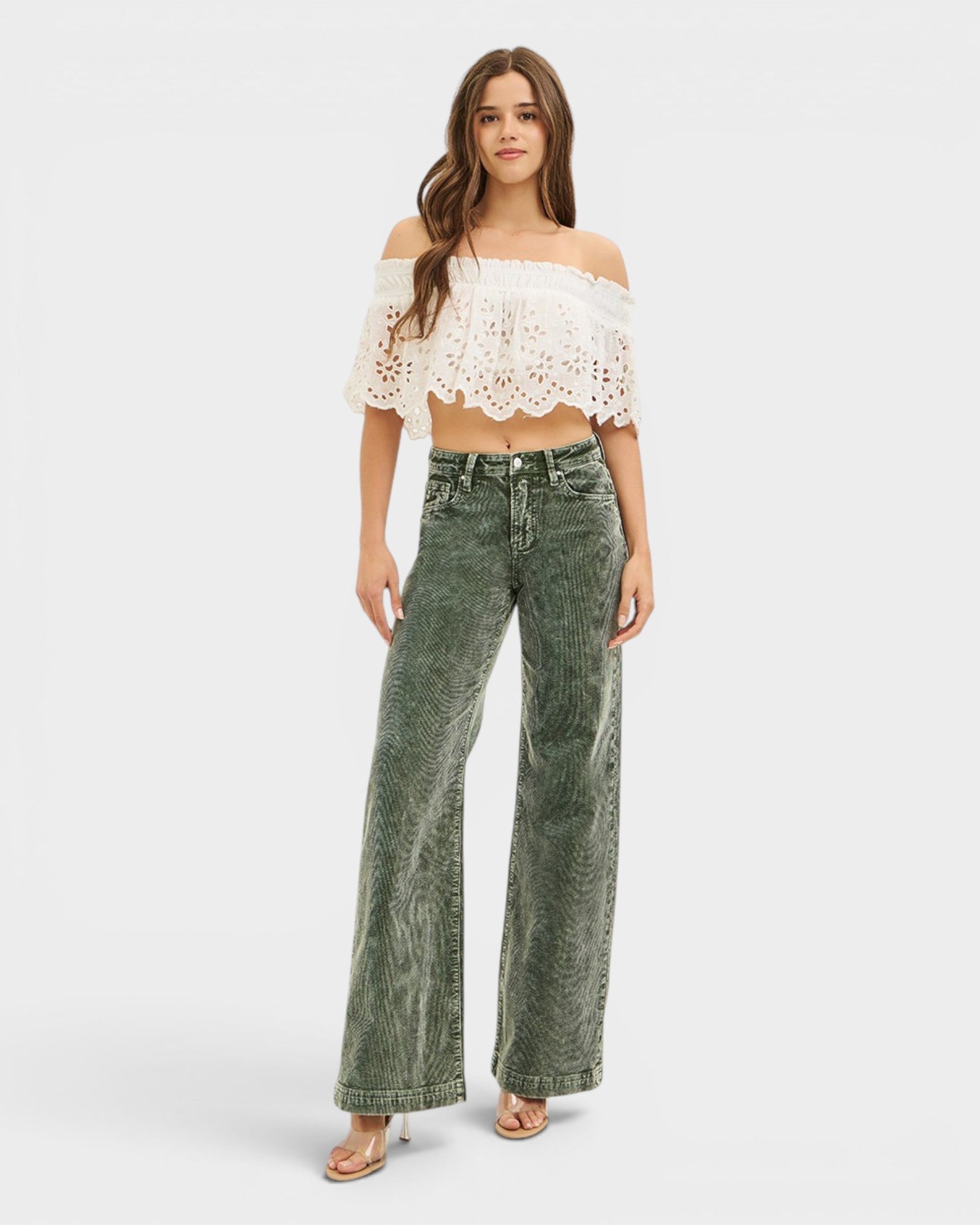 Woman wearing a white lace top and green jeans on a white background
