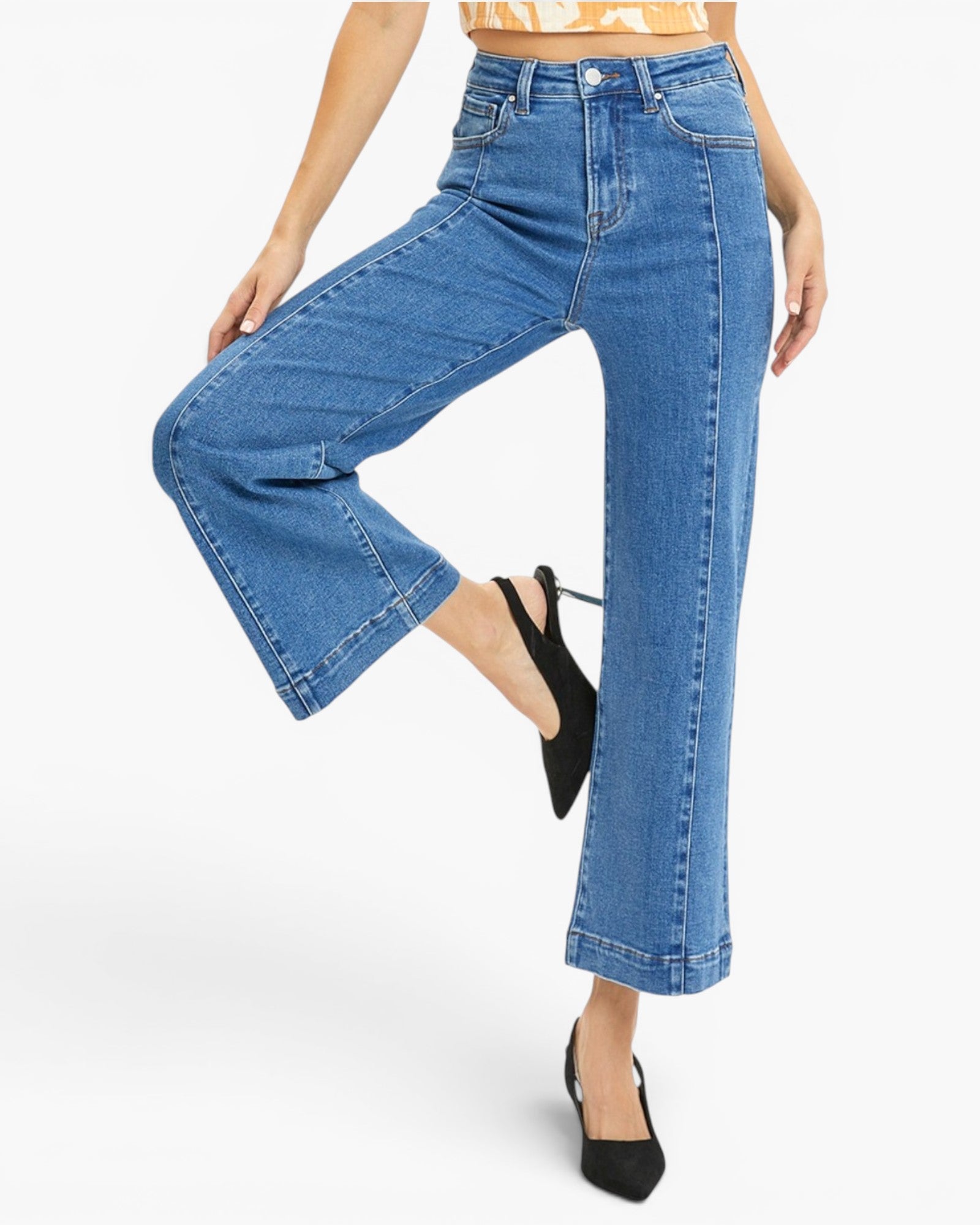 A model wearing a pair of high-waisted, wide-leg cropped blue denim jeans with black slingback heels, shown from the waist down on a light gray studio background.
