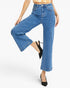 A model wearing a pair of high-waisted, wide-leg cropped blue denim jeans with black slingback heels, shown from the waist down on a light gray studio background.
