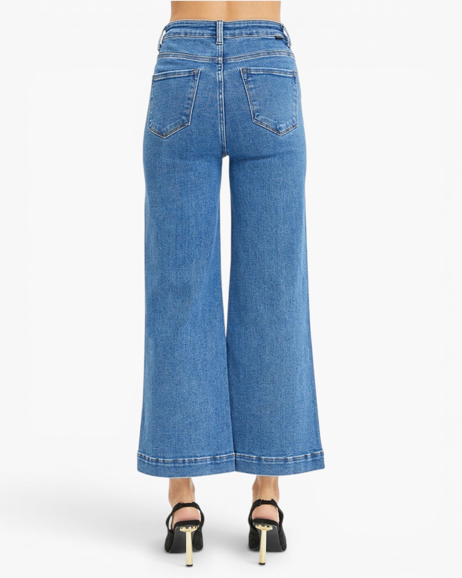 Back view of a model wearing blue wide-leg cropped denim jeans with black high-heeled sandals, shown against a plain white studio background.