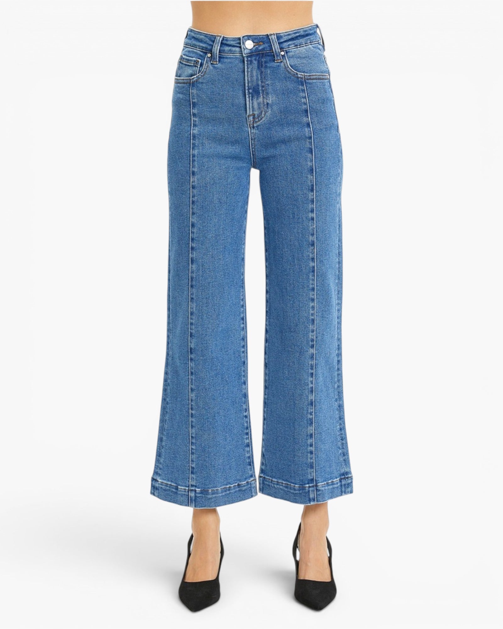 A model is wearing a pair of high-waisted, wide-leg cropped blue denim jeans with black pointed-toe heels, shown against a plain white studio background.