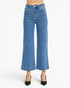 A model is wearing a pair of high-waisted, wide-leg cropped blue denim jeans with black pointed-toe heels, shown against a plain white studio background.