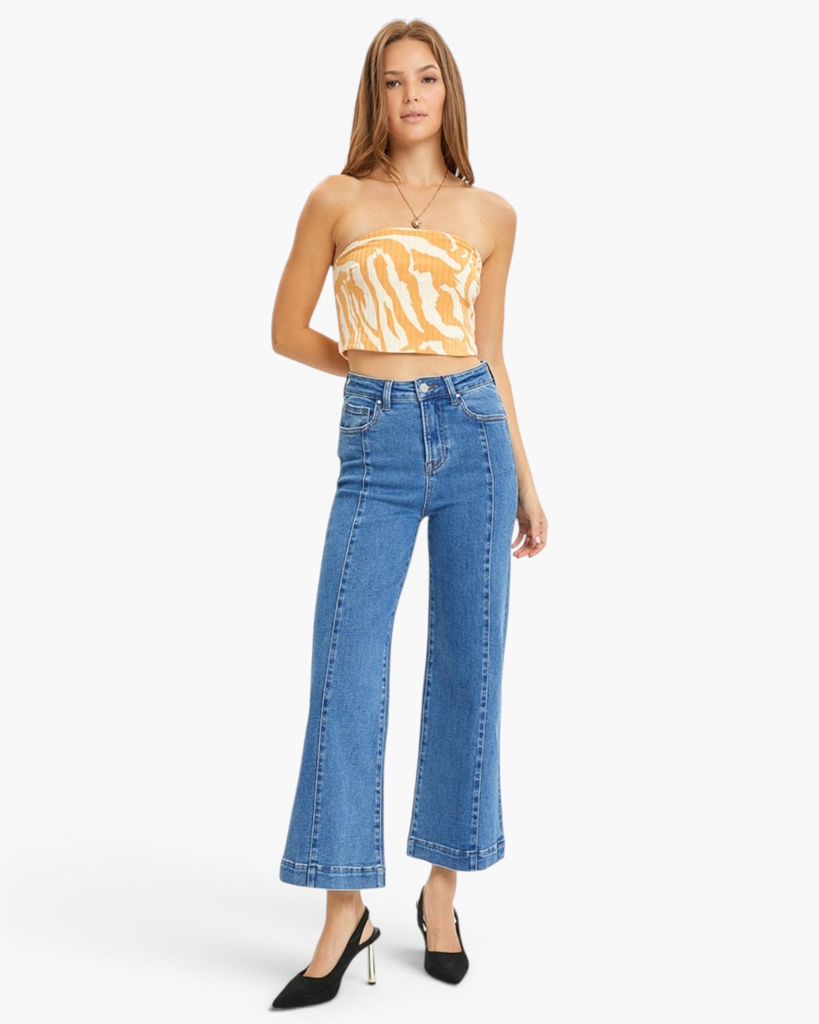 A woman modeling a yellow and white tiger-print strapless tube top and high-waisted, wide-leg blue denim jeans with black pointed-toe heels, set against a plain white studio background.