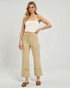 Woman wearing beige pants and a white top on a plain background
