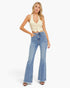 A woman modeling a pair of light-wash blue flare jeans with a cream ribbed crop top against a plain white studio background.