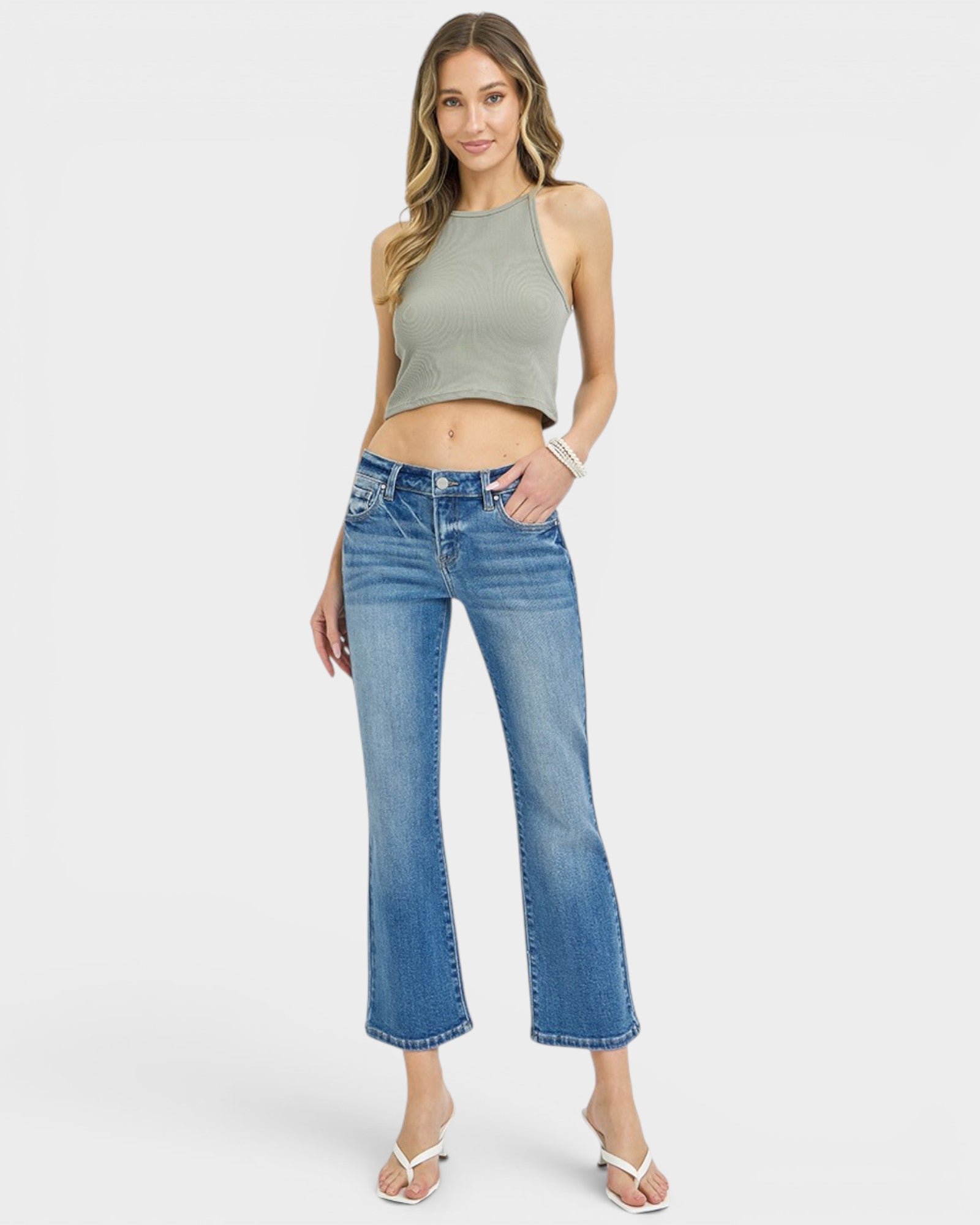 Woman wearing a green tank top and blue jeans on a white background