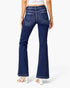 Rear view of a model wearing dark blue flare jeans with a white crop top and white high-heeled sandals against a light gray studio background.