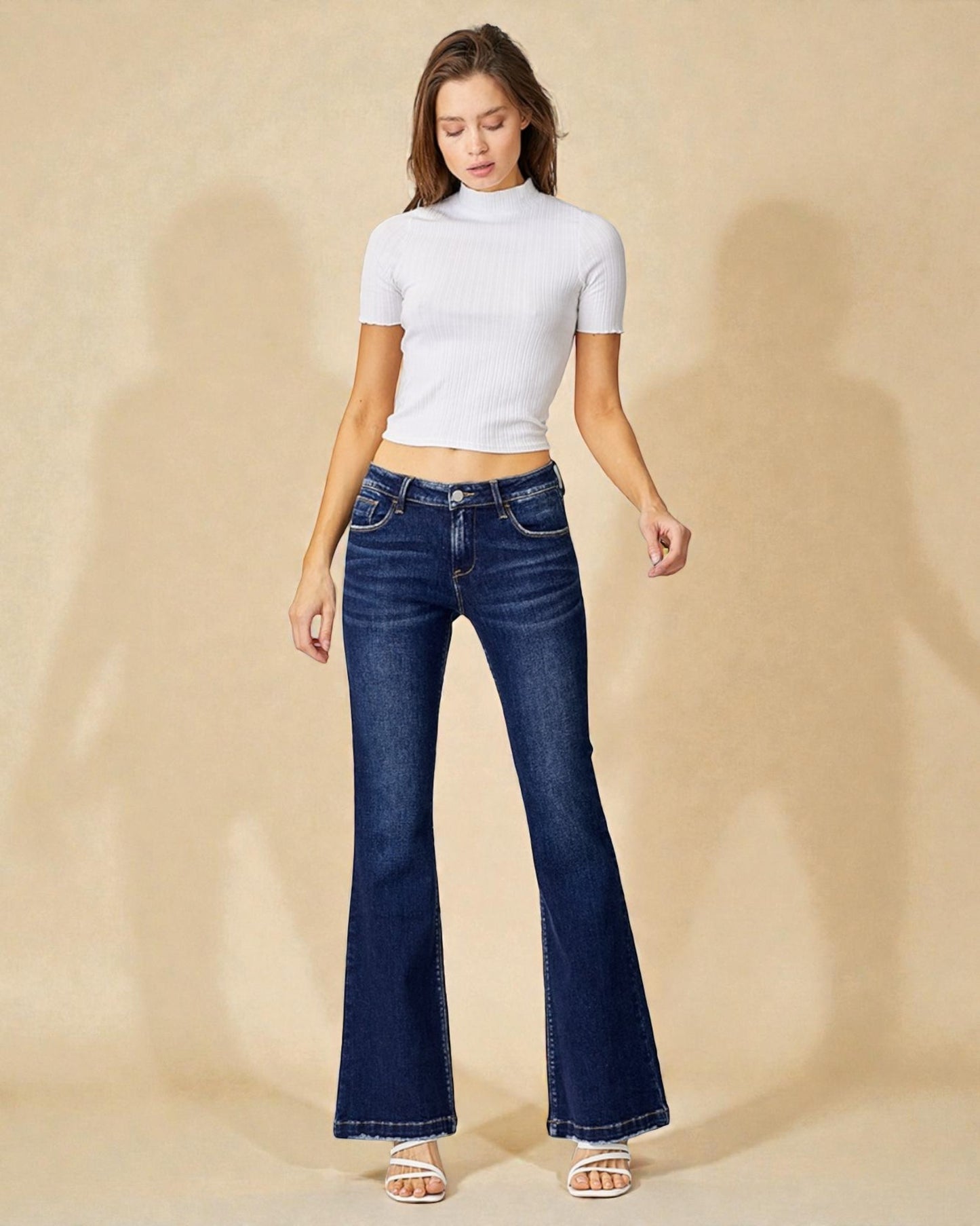 Woman wearing blue flared jeans and a white top on a beige background
