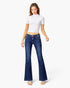 A woman modeling a pair of dark blue low-waisted flare jeans with a white short-sleeve crop top, standing against a light gray studio background.