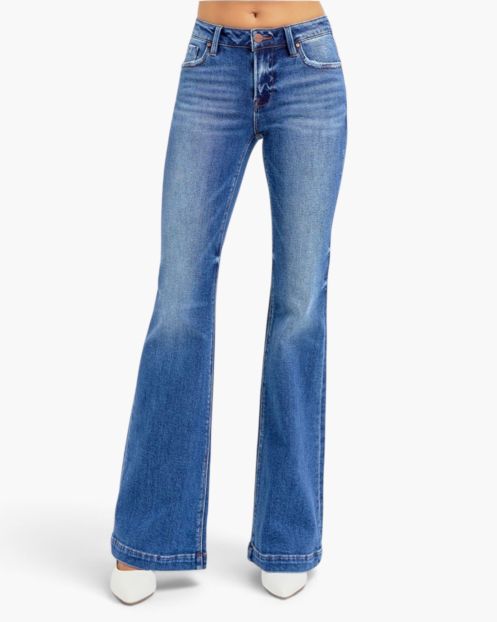 A pair of medium-wash blue denim flare jeans shown on a model from the waist down, paired with white pointed shoes against a plain white studio background.
