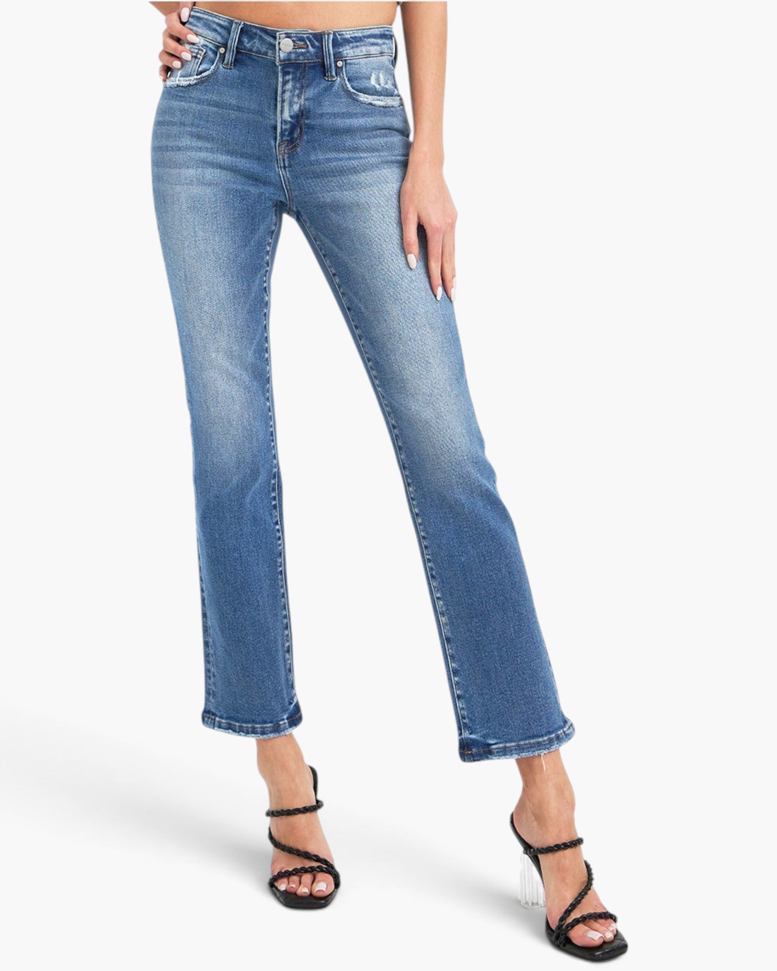 A model wearing a pair of medium-wash blue denim jeans with a straight-to-ripped leg and rolled hems, paired with black strappy high-heeled sandals against a plain white studio background.