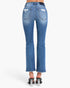 Rear view of a model wearing blue denim flare jeans with distressed details on the back pockets and frayed hems, paired with black high-heeled sandals against a plain white background.