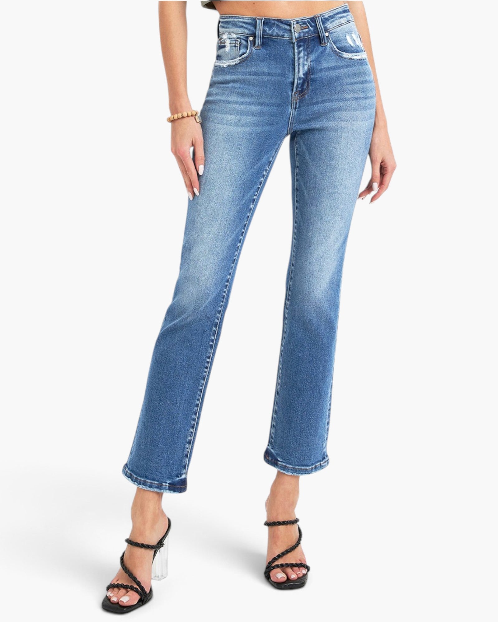 A model wearing a pair of medium-wash blue denim jeans with a straight-to-crew leg, styled with black strappy high-heeled sandals against a clean white background.