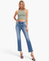 A woman modeling a sleeveless sage green ribbed crop top and blue cropped flare jeans with black strappy heels, photographed against a clean white studio background.