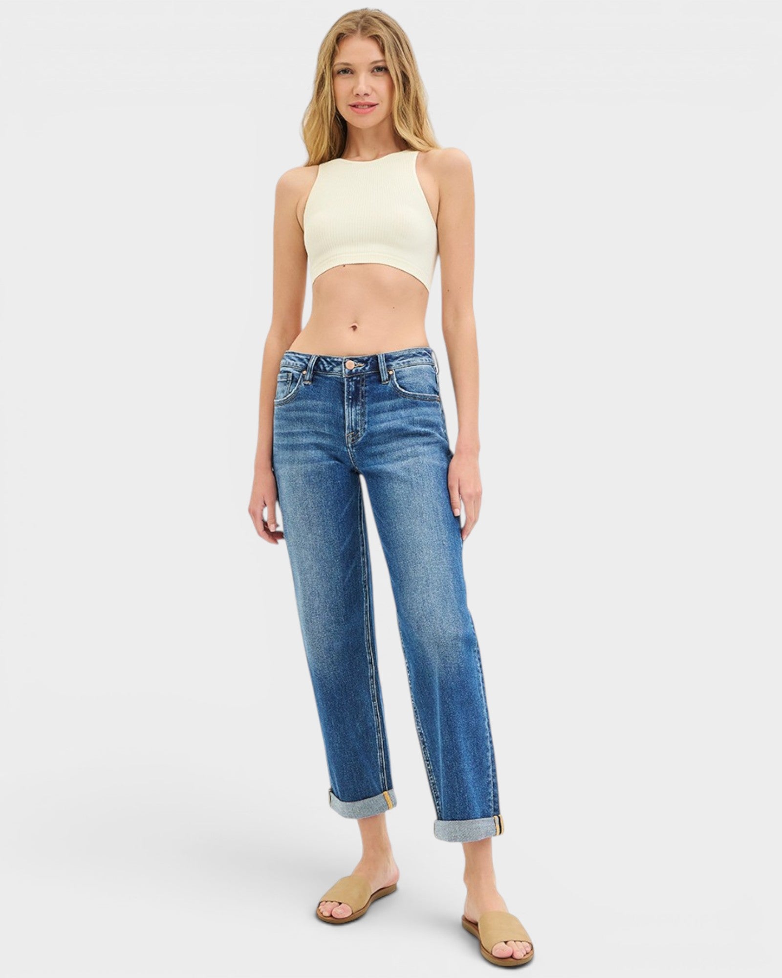 Woman wearing a light-colored crop top and blue jeans on a white background