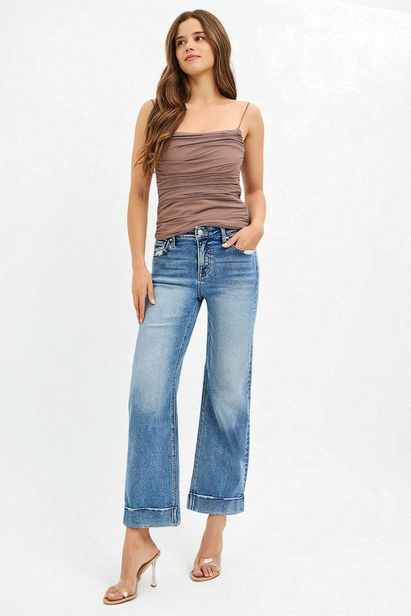 Woman wearing a brown tank top and blue jeans on a white background