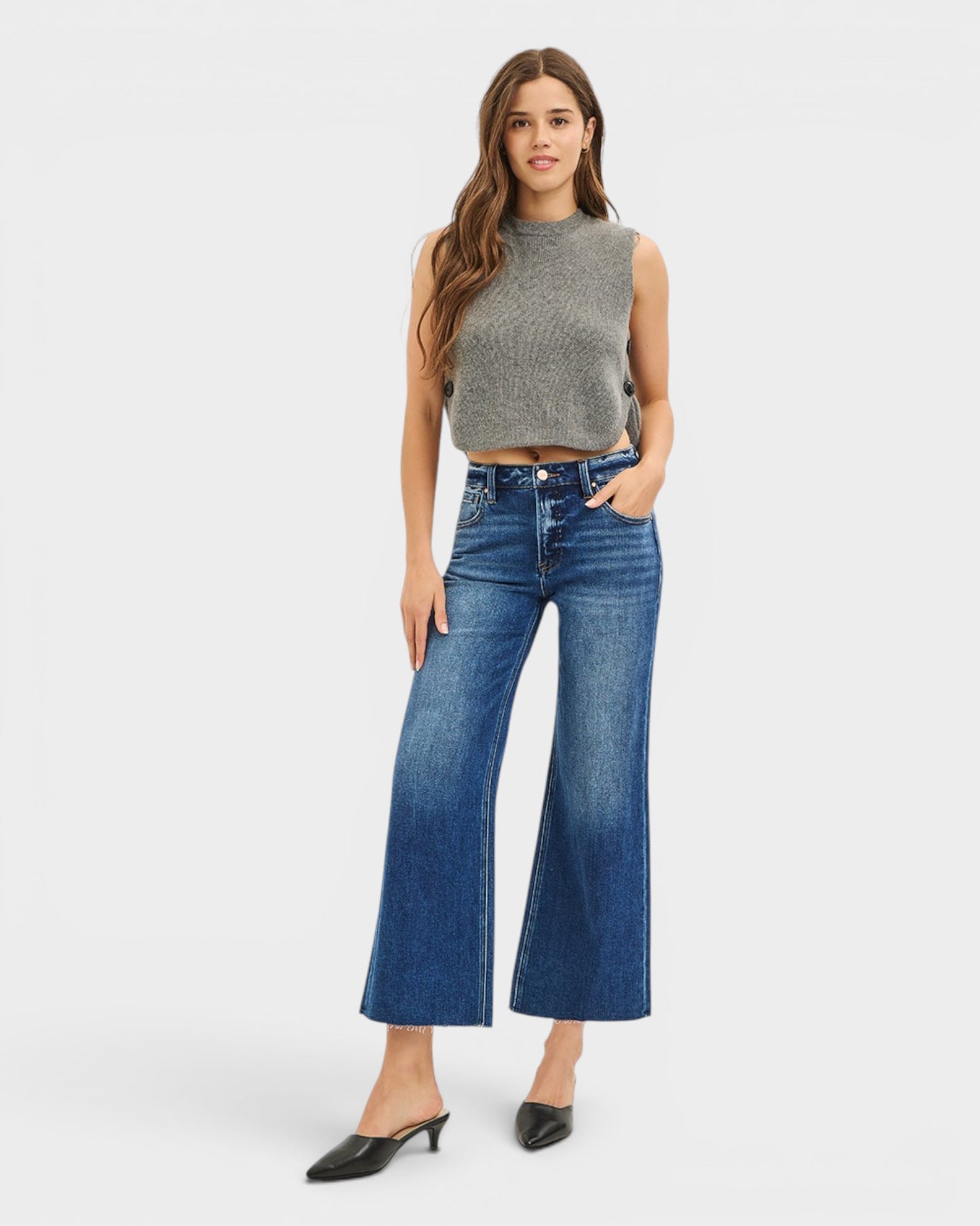 Woman wearing a sleeveless gray top and blue jeans on a white background