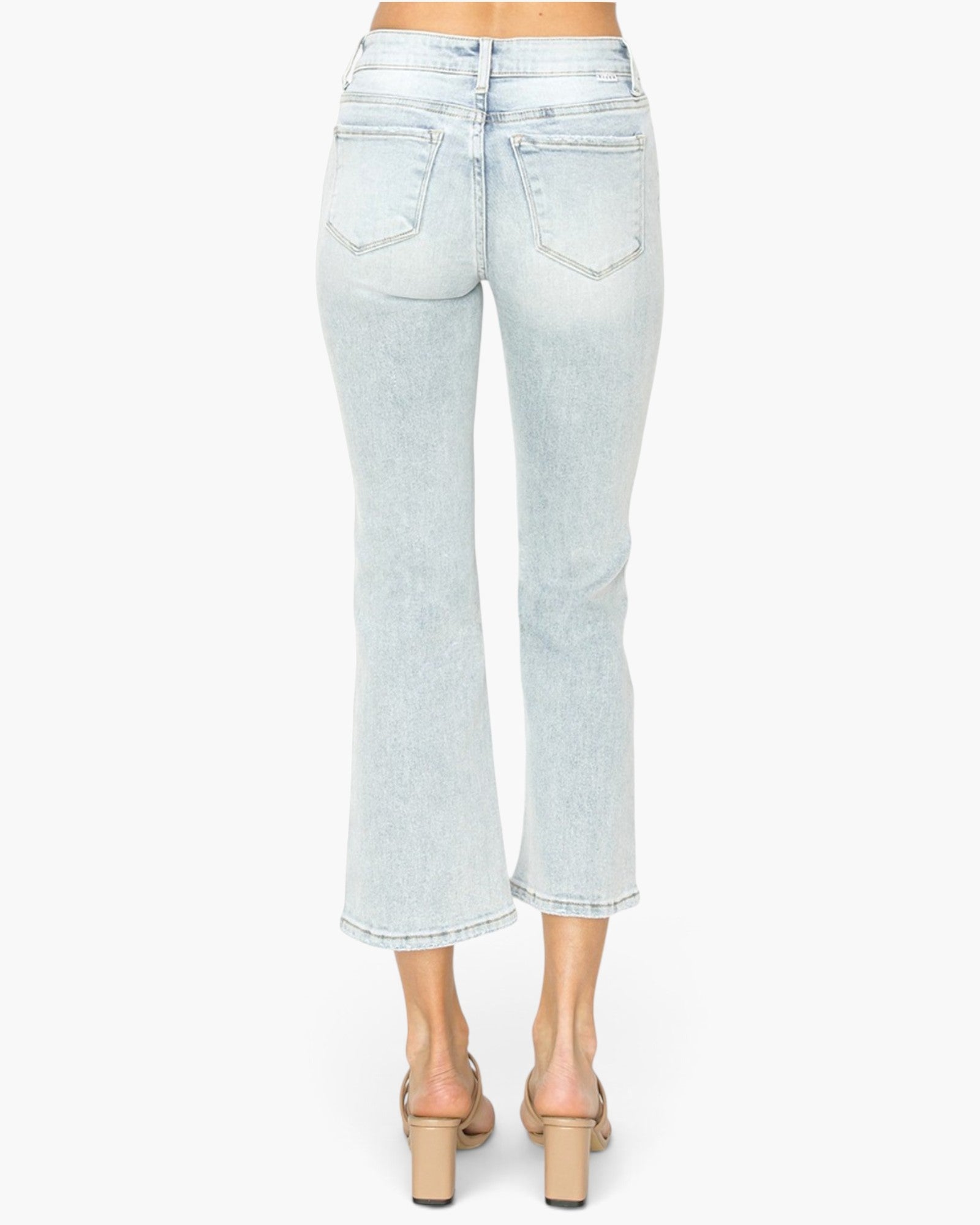 Light wash blue cropped flare jeans shown from the back on a model, paired with beige block-heel mules against a plain white background.