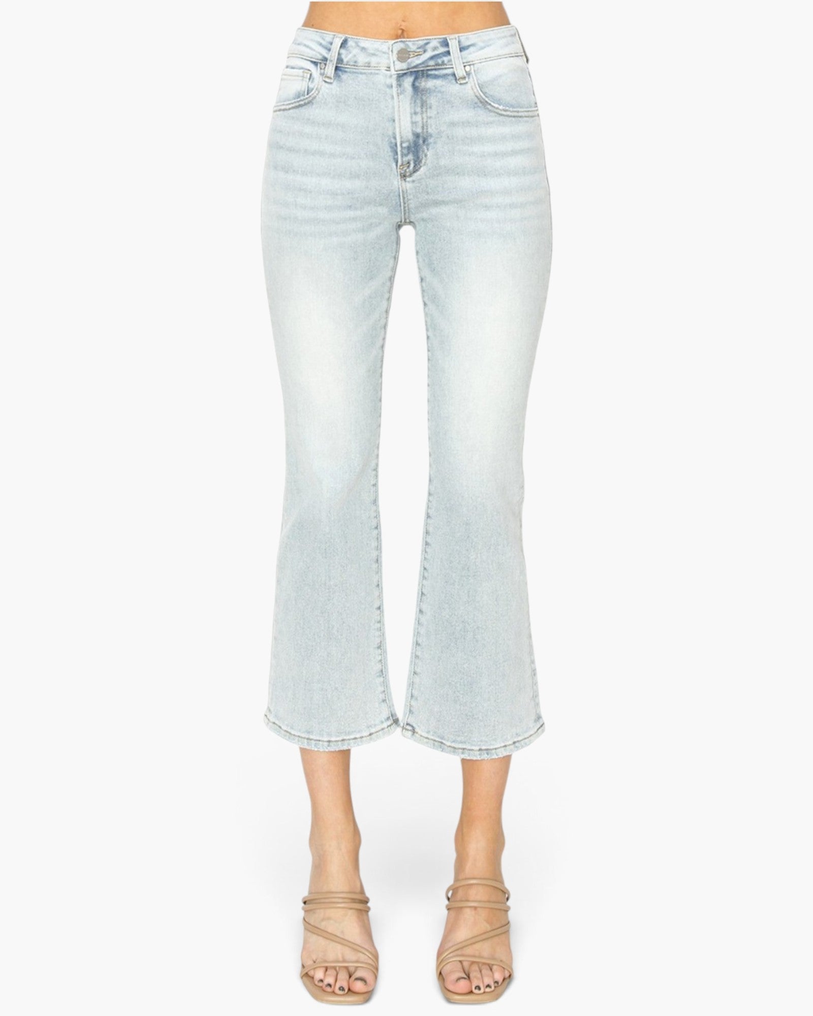 Light-wash cropped flare jeans shown on a model from the waist down, paired with beige strappy heeled sandals against a plain white background.