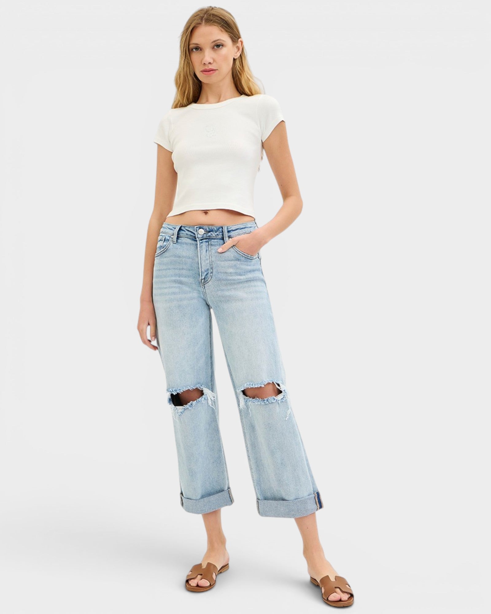 Woman wearing a white crop top and light blue jeans with rips on a white background