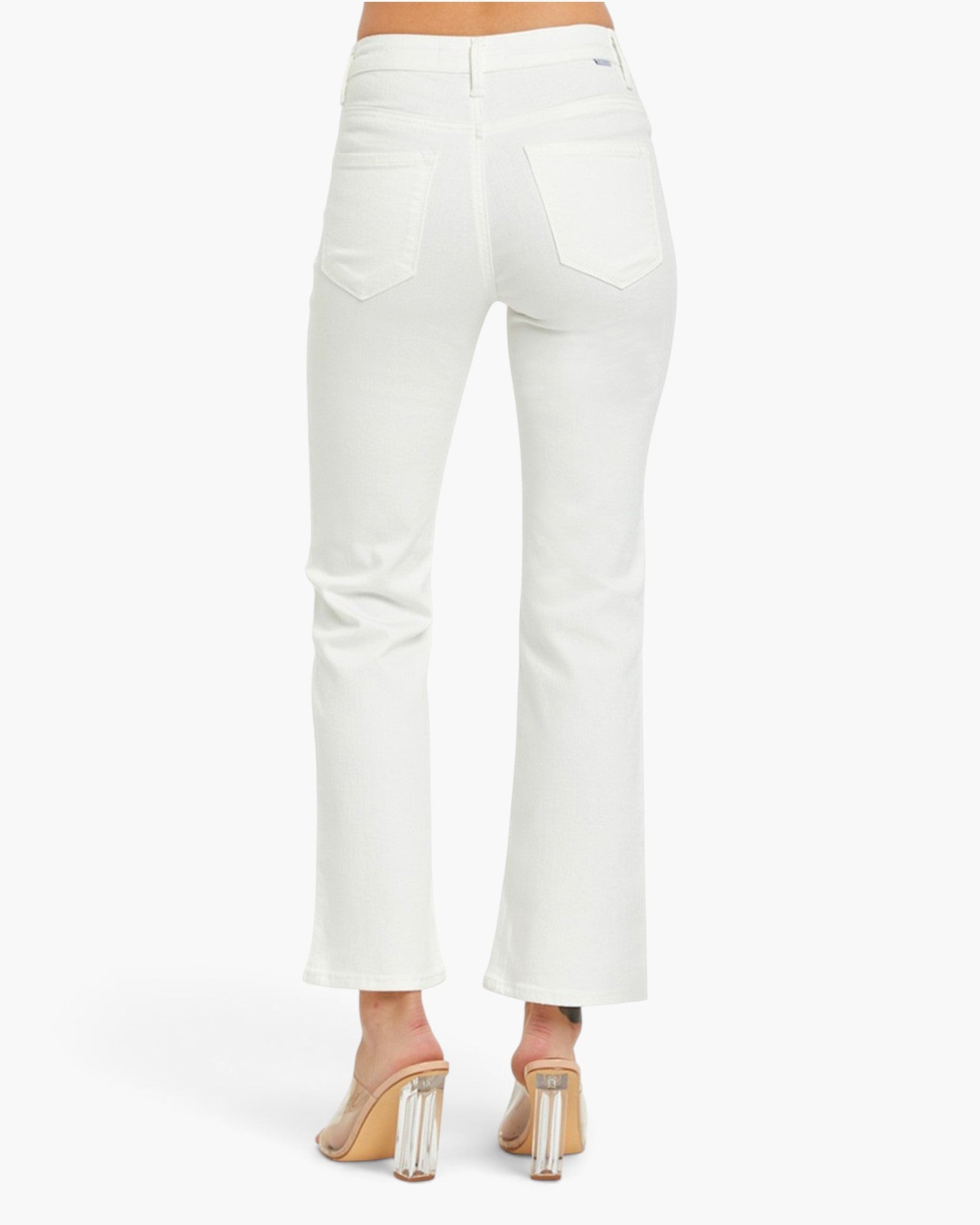 White cropped flare jeans shown from the back on a model, paired with clear high-heeled mules, against a clean white studio background.