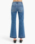 Rear view of a person wearing blue wide-leg denim jeans with a straight-to-flared leg and black block-heel sandals against a light gray studio background.