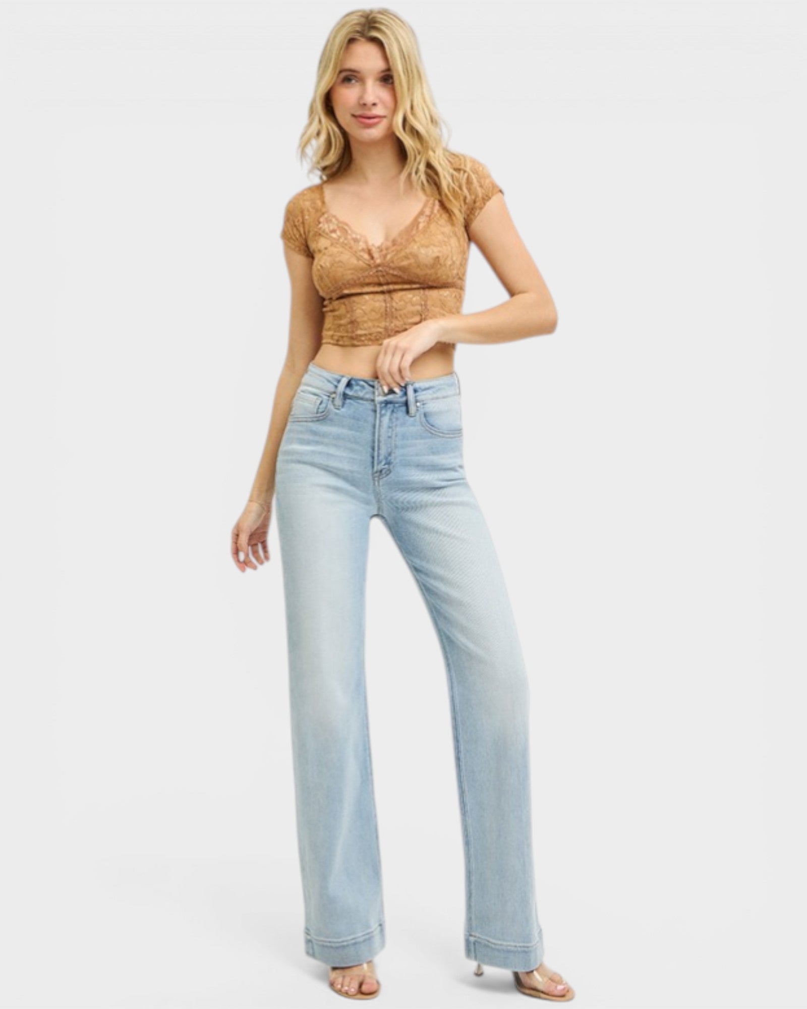 Woman wearing a brown lace top and light blue jeans on a white background