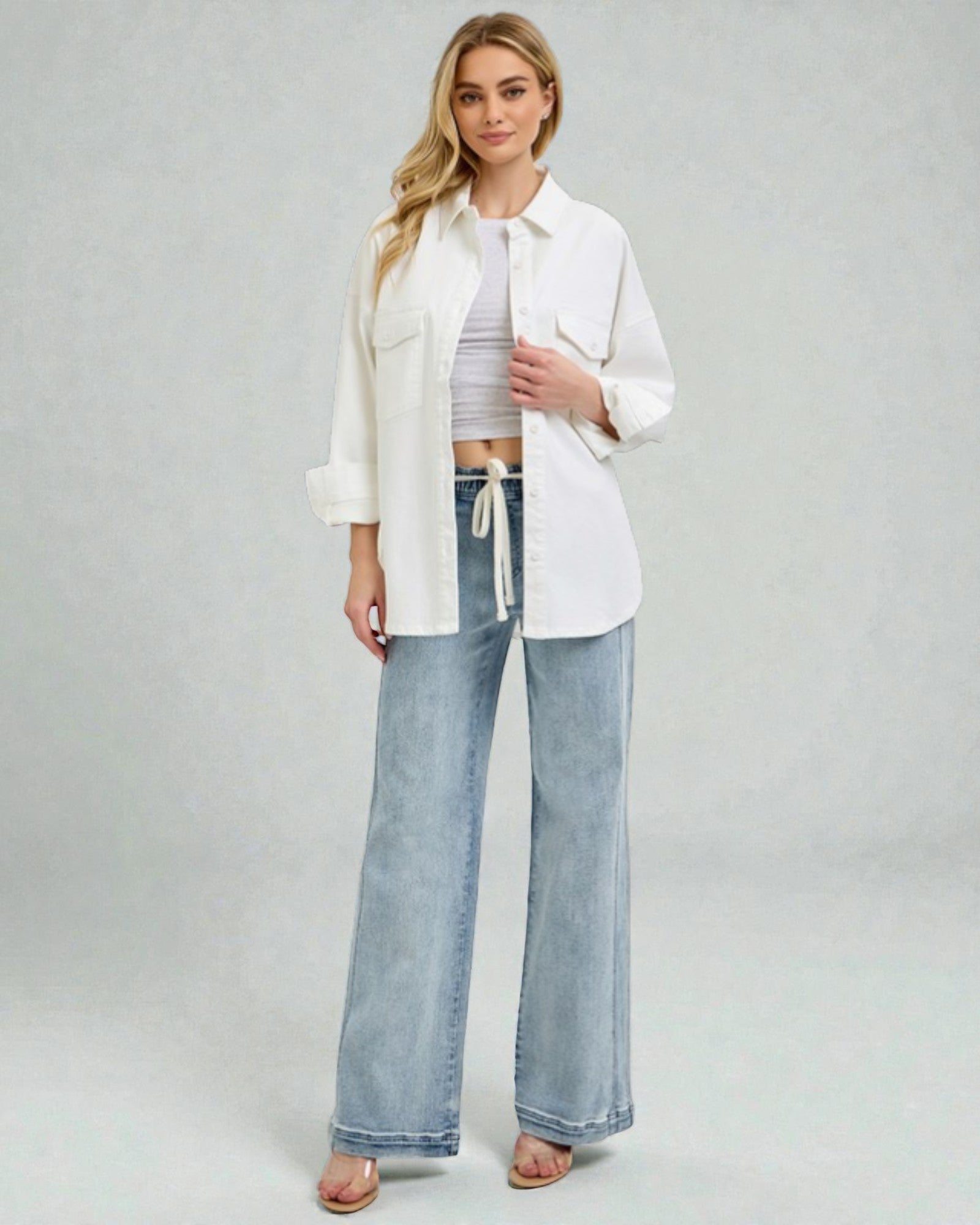 Woman wearing a white shirt, gray top, and blue jeans on a plain background