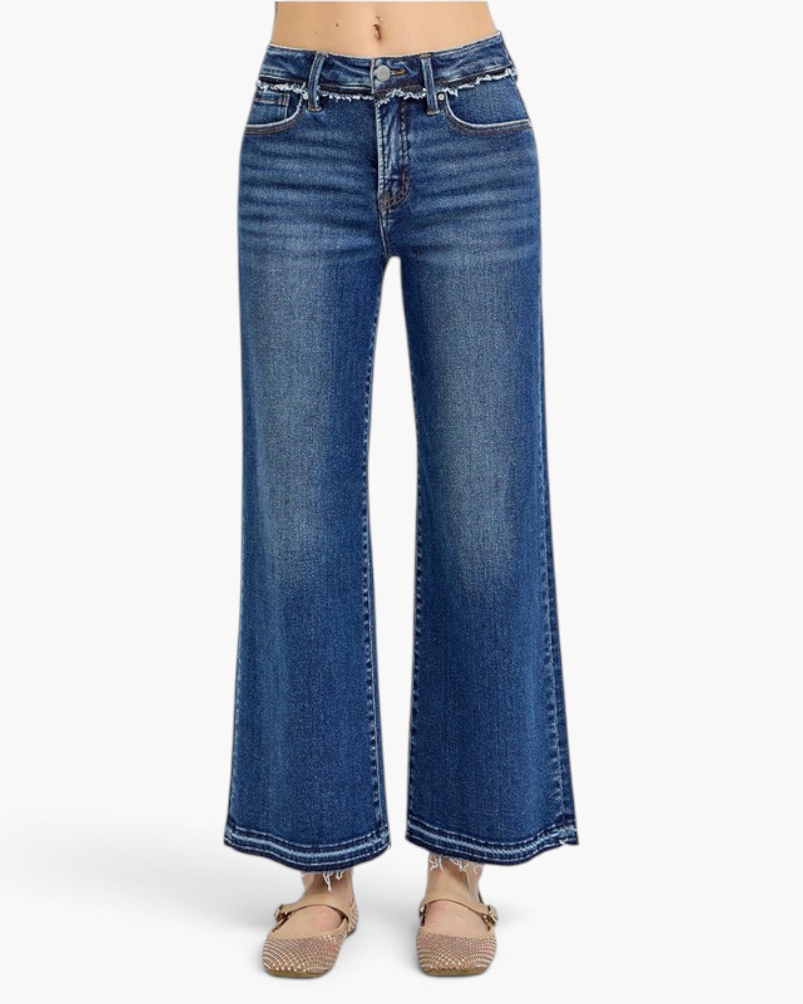 A person wearing blue wide-leg denim jeans with a frayed waistband and beige flat sandals, shown from the waist down against a light gray studio background.