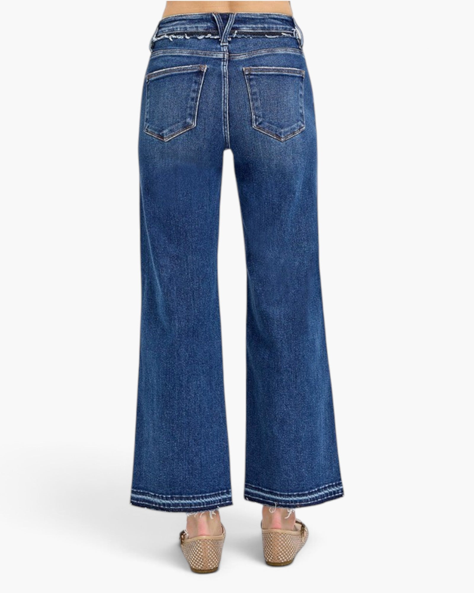 Back view of a model wearing blue wide-leg jeans with contrast stitching and wedge sandals, shown against a plain white studio background.