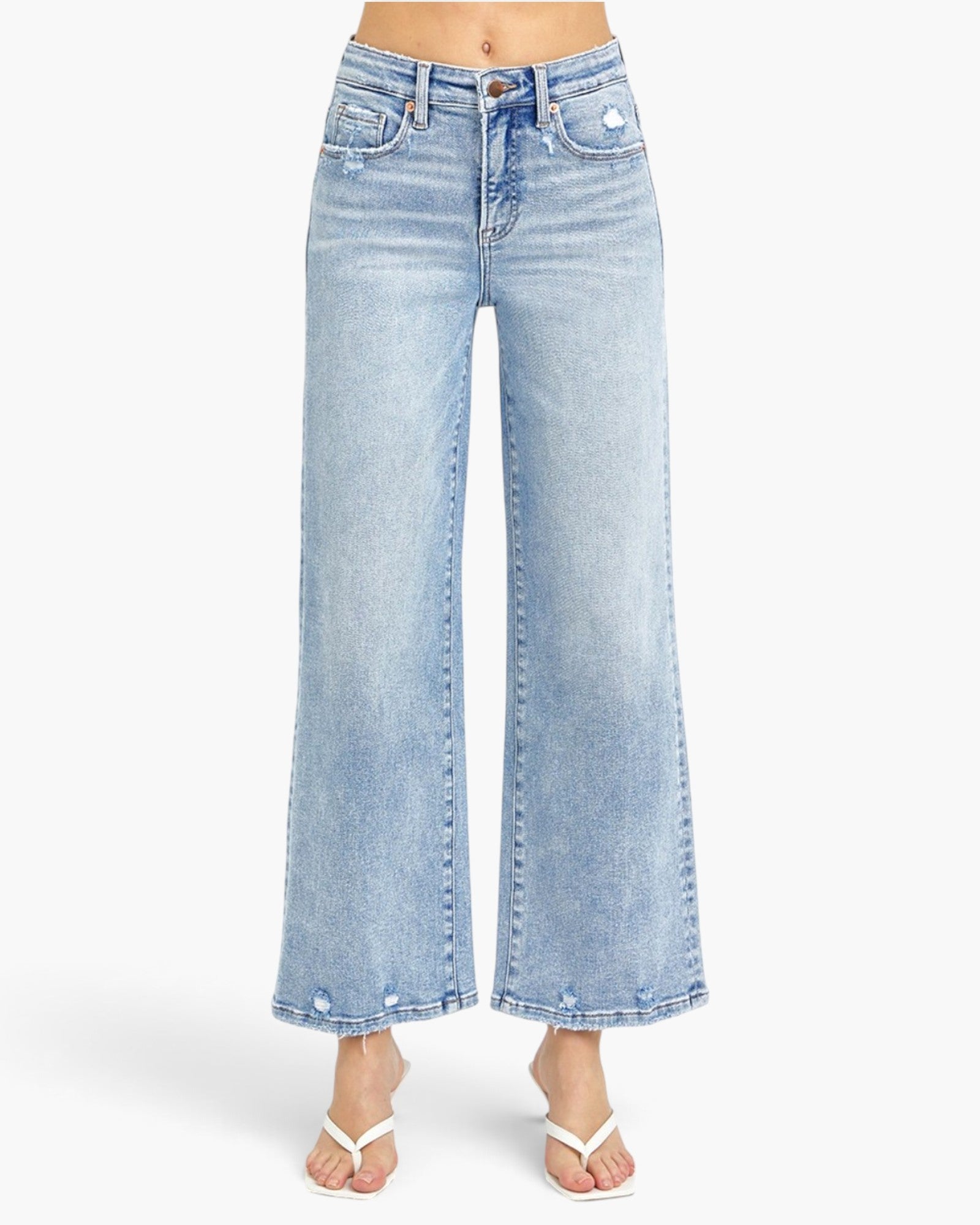 A person wearing light-wash blue wide-leg cropped jeans with a faded wash and white thong sandals, shown against a plain light gray studio background.
