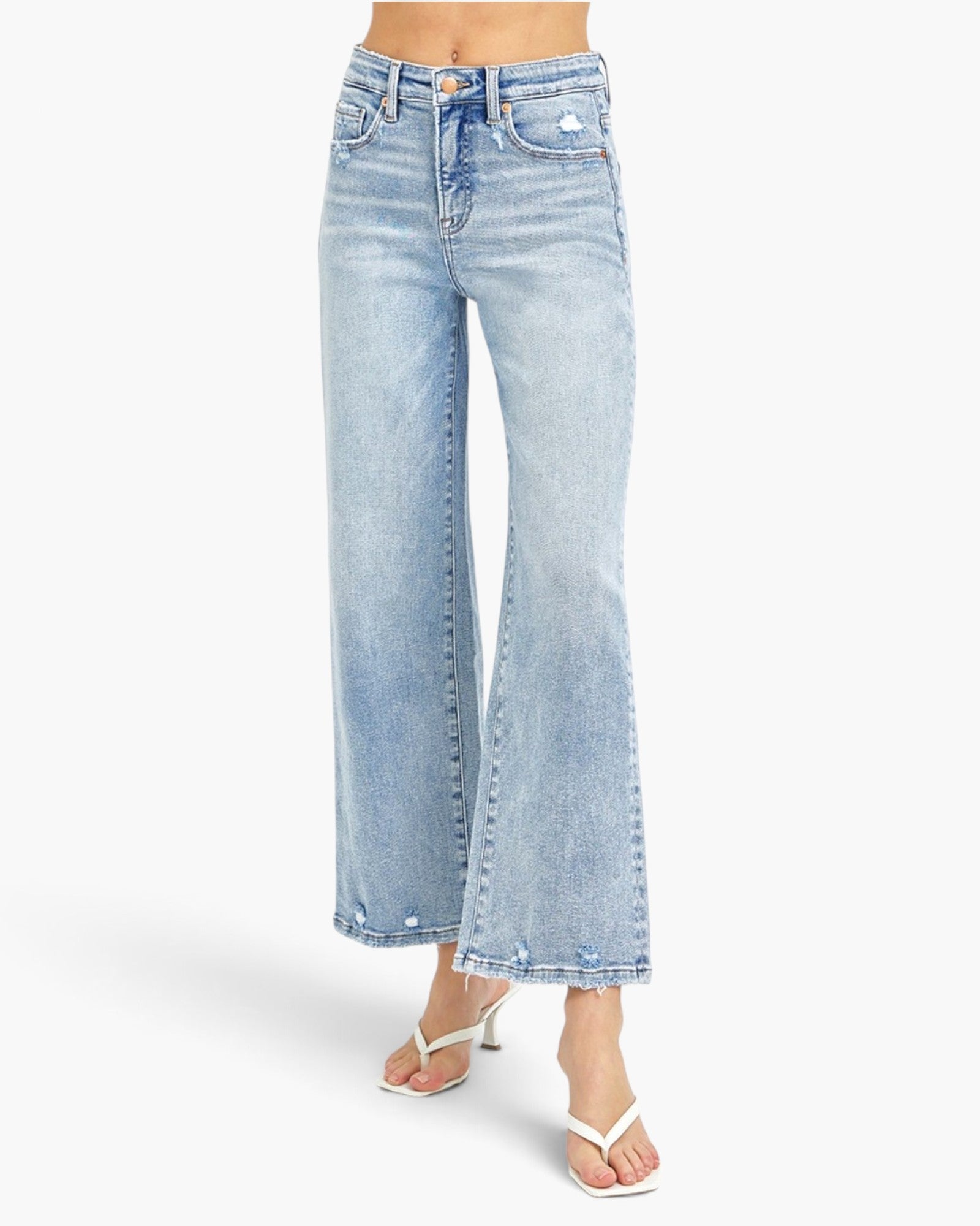 A model from the waist down wearing light-wash blue wide-leg cropped jeans and white heeled thong sandals, set against a plain white studio background.