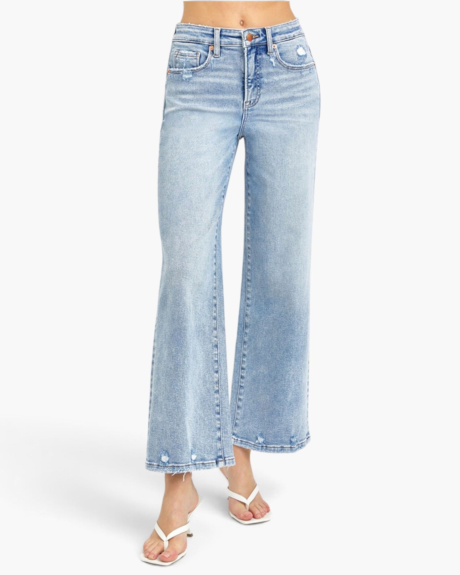 A model wearing light-wash blue wide-leg cropped jeans with silver rivets and white thong sandals, shown from the waist down on a light gray studio background.
