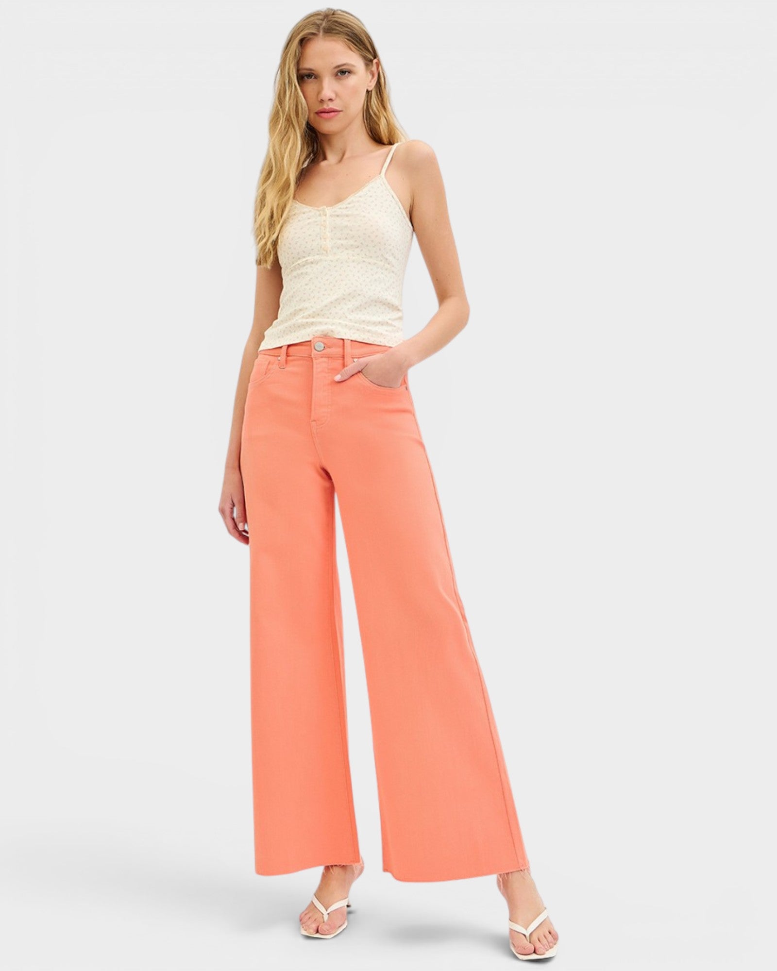 Woman wearing a white tank top and coral wide-leg pants on a light gray background