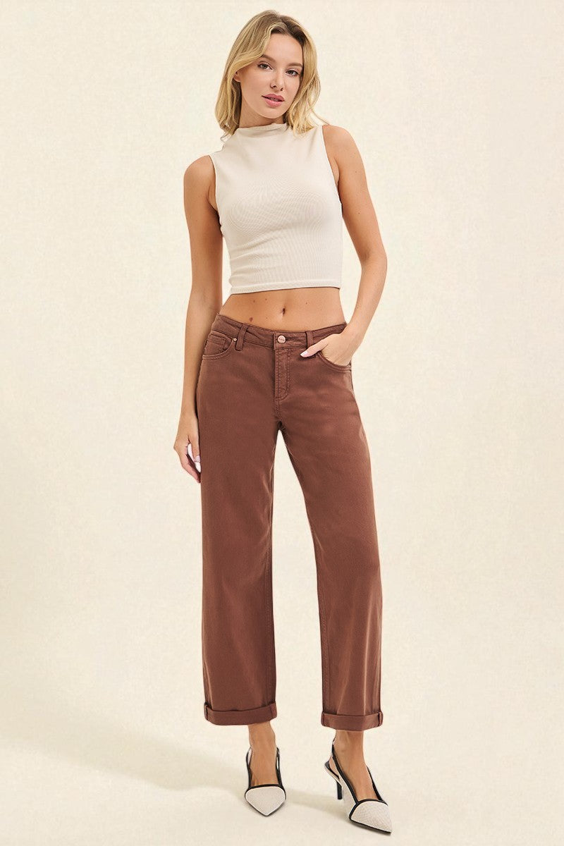 Woman wearing a white sleeveless top and brown high-waisted jeans on a beige background