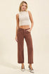 Woman wearing a white sleeveless top and brown high-waisted jeans on a beige background